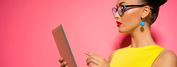 Fashionable lady in yellow in front of a pink background reading about IT marketing on a green tablet.